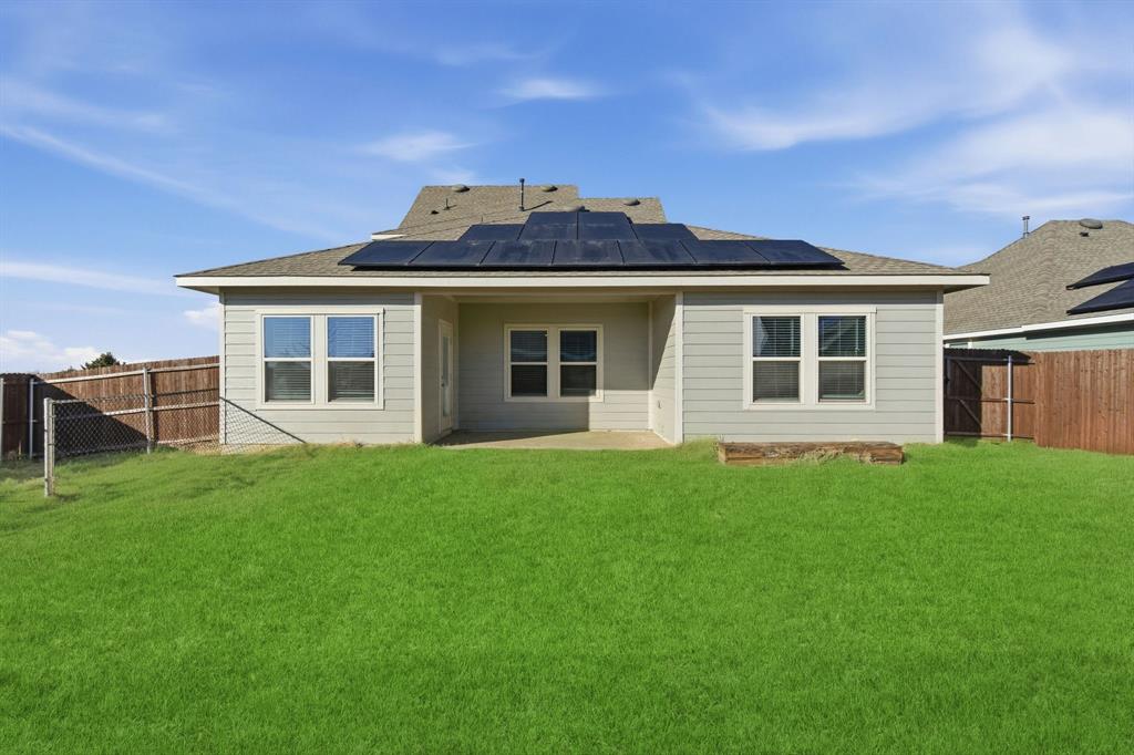709 Primrose Lane Pilot Point, TX 76258 - Photo 27 of 35 Rear view of house with a fenced backyard, a patio area, roof mounted solar panels, and a shingled roof