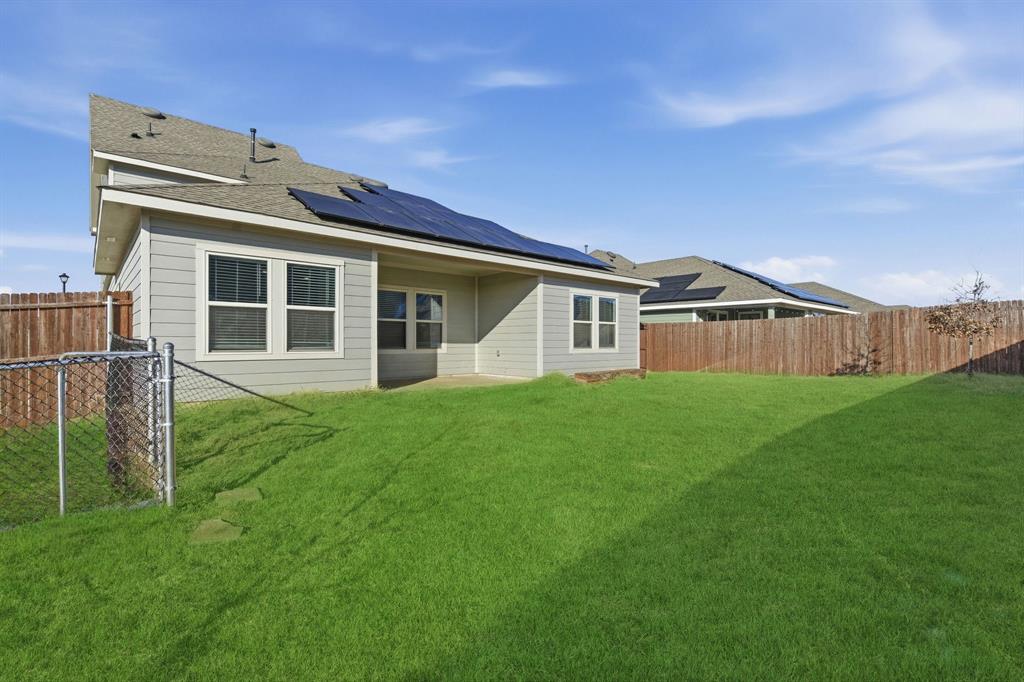 709 Primrose Lane Pilot Point, TX 76258 - Photo 28 of 35 Rear view of house with a fenced backyard, a shingled roof, solar panels, and a patio area