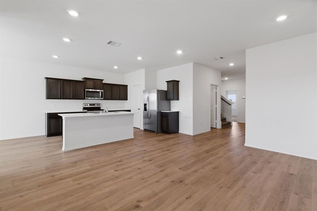 709 Primrose Lane Pilot Point, TX 76258 - Photo 32 of 35 Kitchen featuring open floor plan, light countertops, stainless steel appliances, dark wood finish cabinets, and light wood-style floors