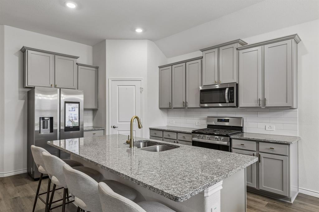 10313 Geode Street Aubrey, TX 76227 - Photo 3 of 13 Kitchen featuring a large island with granite countertops, stainless steel appliances, a subway tile backsplash, and light gray cabinetry