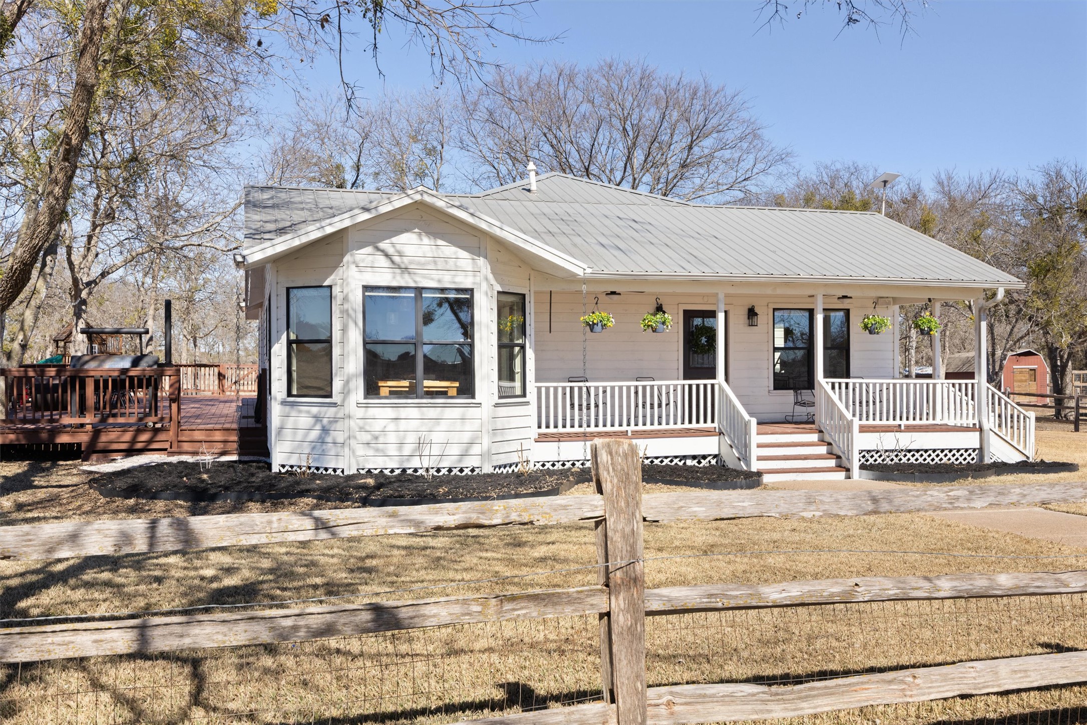 13590 Ranch Road 2338 Georgetown, TX 78633 - Photo 2 of 39 Single story cedar farmhouse with a metal roof, large covered entry deck and extended deck with seating area on the side, perfect for large gatherings and cook outs under the trees! The main house was recently painted white in 2026.
