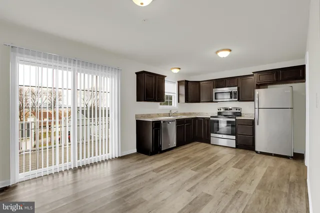 a kitchen with stainless steel appliances a refrigerator a sink dishwasher a oven with white cabinets and wooden floor