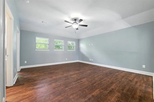 an empty room with wooden floor ceiling fan and windows