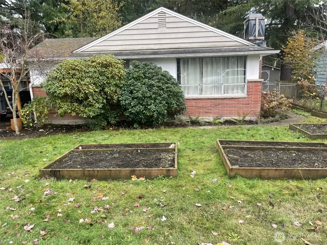a view of a white house with a yard plants and large tree