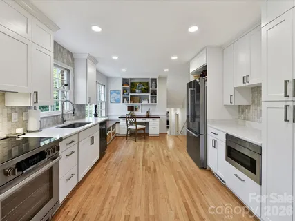 a kitchen with stainless steel appliances a stove a sink dishwasher a refrigerator white cabinets and wooden floor