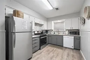 a kitchen with stainless steel appliances granite countertop a refrigerator a sink dishwasher a stove top oven a refrigerator with white cabinets and wooden floor