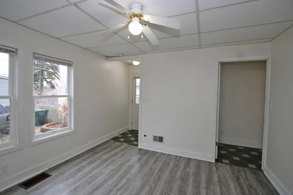 an empty room with wooden floor chandelier fan and windows