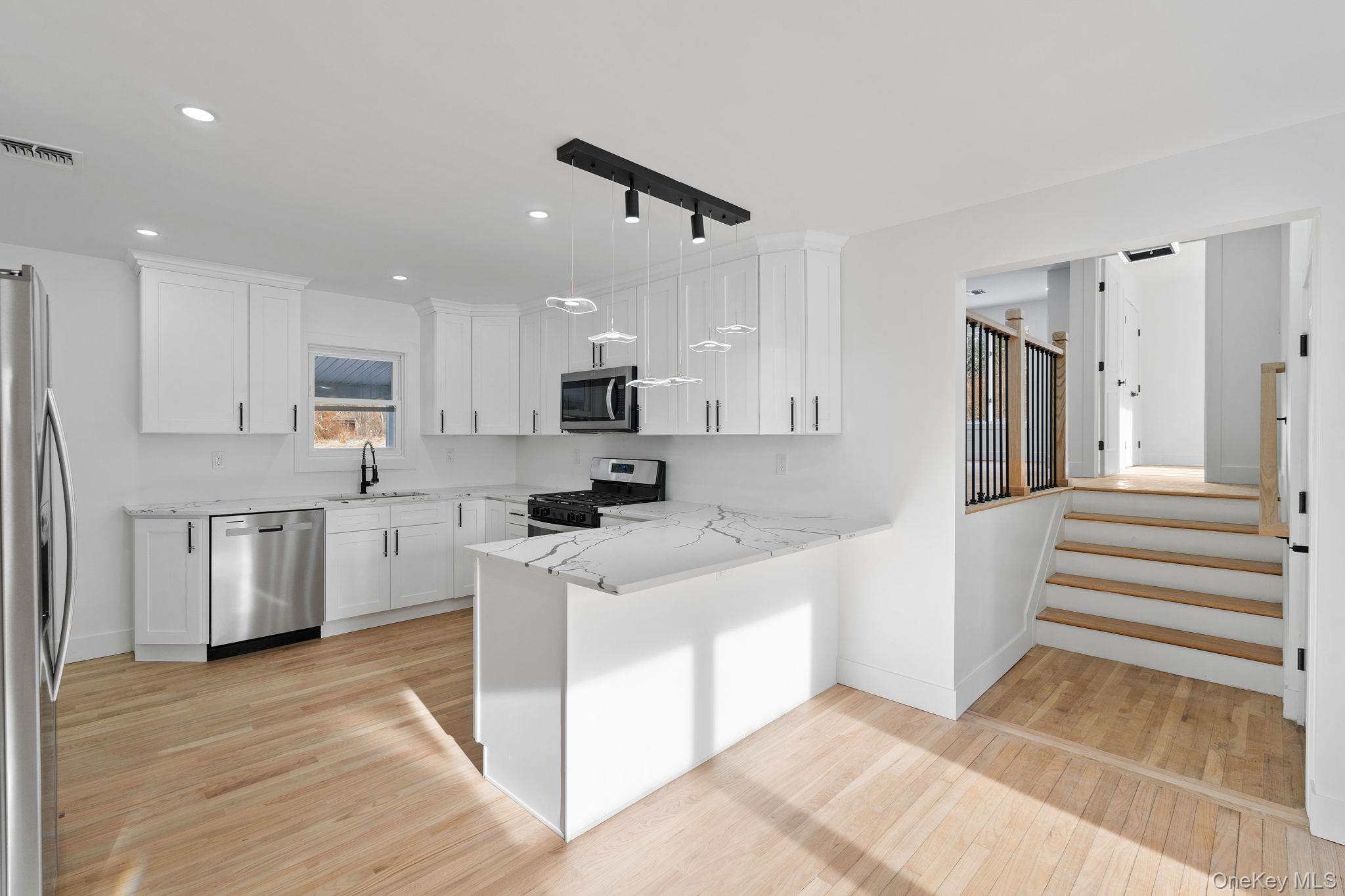 52 Rudolph Road Modena, NY 12548 - Photo 6 of 49 Kitchen featuring appliances with stainless steel finishes, white cabinets, a peninsula, decorative light fixtures, and light wood-type flooring