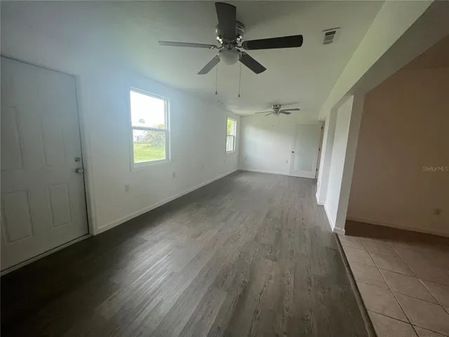 an empty room with wooden floor fan and windows