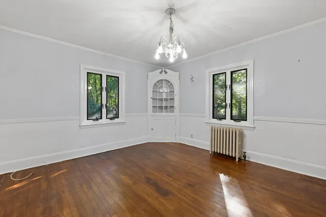 an empty room with wooden floor chandelier and windows