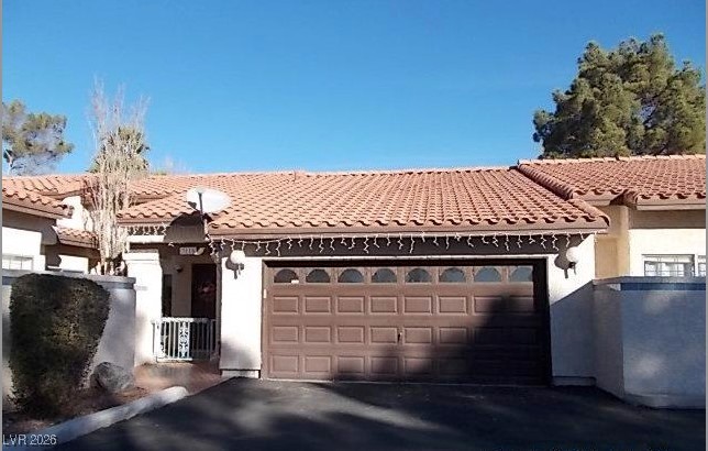 Mediterranean / spanish-style house with stucco siding, driveway, an attached garage, and a tile roof