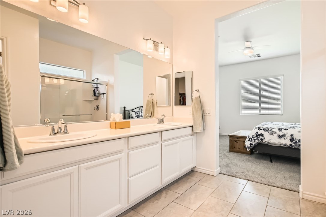 498 Pebble Run Avenue Henderson, NV 89011 - Photo 14 of 47 This primary bathroom features a dual vanity, a large mirror, and tiled flooring, with a clear view into the adjacent carpeted bedroom.