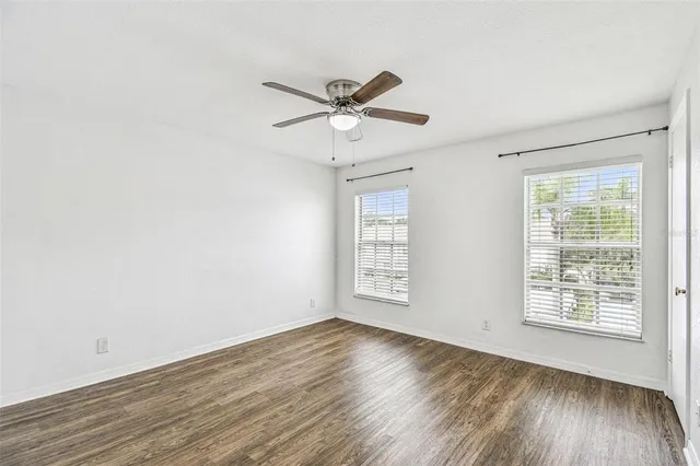 an empty room with wooden floor fan and windows