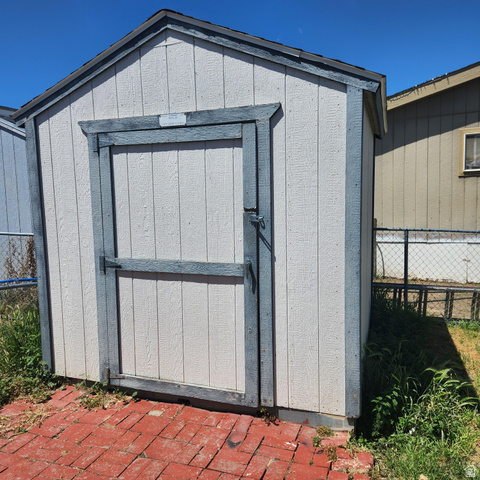 3760 Gold Ridge Drive, Unit 82 Magna, UT 84044 - Photo 8 of 29 Gable-roofed storage shed with vertical panel siding, a wood-framed door with strap hinges, and a red brick paver base