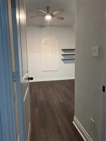 a view of an empty room with wooden floor and a ceiling fan