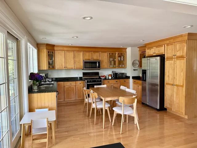 a kitchen with stainless steel appliances granite countertop a refrigerator a stove a kitchen island and chairs with wooden floor