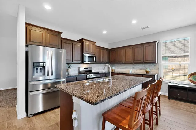 a kitchen with stainless steel appliances granite countertop a sink a stove a refrigerator a center island and a window