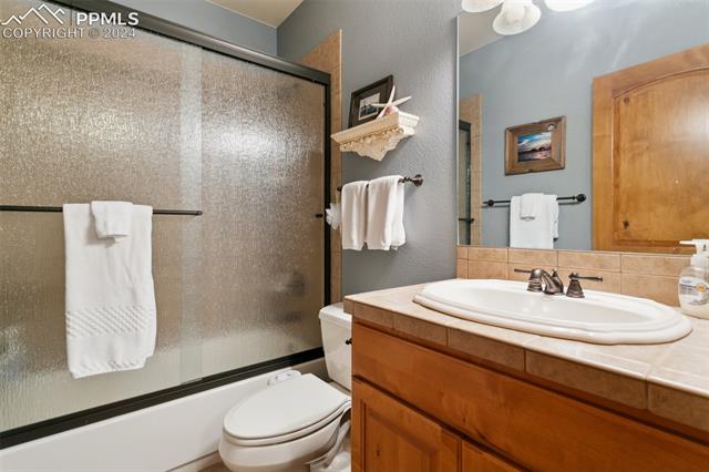 5470 Roundup Ridge Road Colorado Springs, CO 80908 - Photo 19 of 21 Full bathroom featuring toilet, shower / bath combination with glass door, backsplash, and oversized vanity