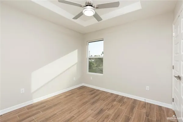 an empty room with wooden floor chandelier fan and windows