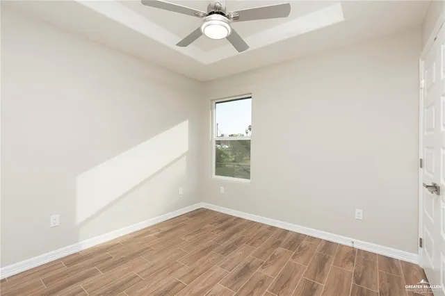 an empty room with wooden floor chandelier fan and windows