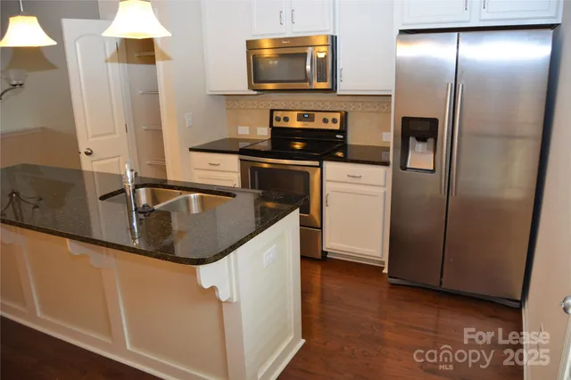 a kitchen with stainless steel appliances granite countertop a refrigerator a stove and a sink with wooden floor
