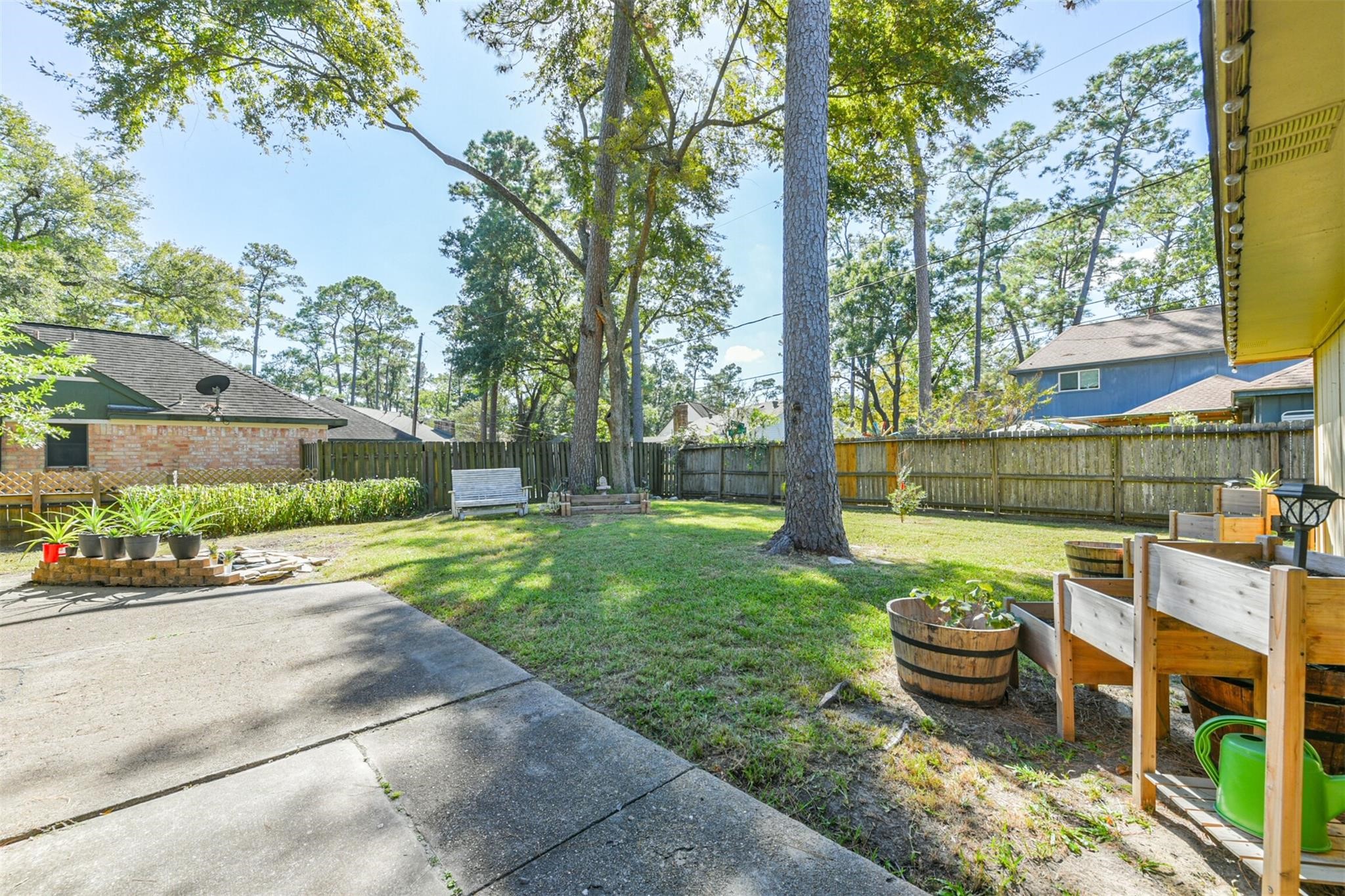 3728 Autumn Lane Baytown, TX 77521 - Photo 14 of 16 A spacious backyard featuring a mix of lawn and paved areas, bordered by a wooden fence. It includes mature trees providing shade, a small garden area, and a cozy, ideal for relaxation and outdoor activities.