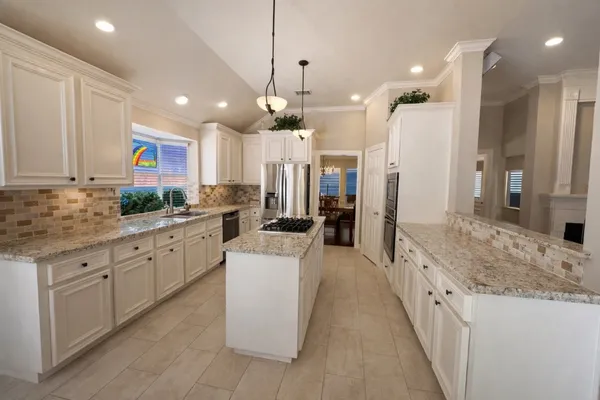 a large kitchen with stainless steel appliances kitchen island granite countertop a sink and a refrigerator