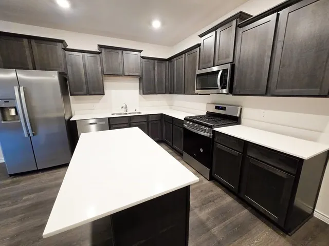 a kitchen with granite countertop a refrigerator a sink a stove a microwave and wooden cabinets