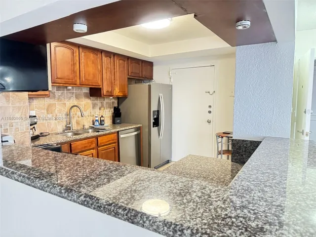 a kitchen with stainless steel appliances kitchen island granite countertop a sink refrigerator and cabinets