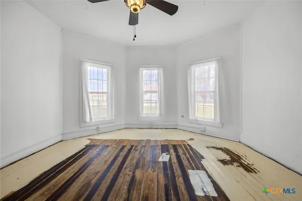 an empty room with wooden floor chandelier fan and windows
