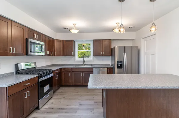 a kitchen with stainless steel appliances granite countertop a sink a stove top oven a refrigerator cabinets and wooden floor