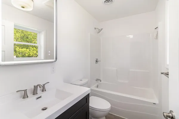 a bathroom with a bathtub shower sink vanity mirror and toilet