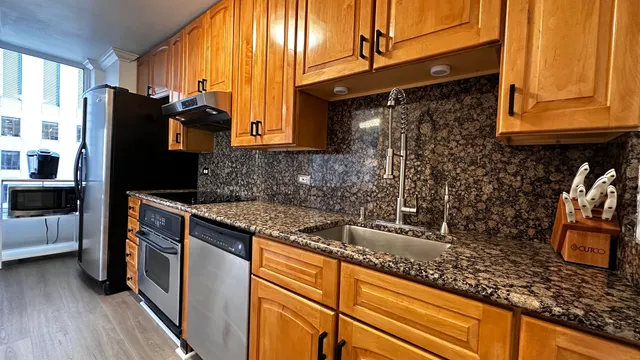 a kitchen with granite countertop a sink a counter top space cabinets and stainless steel appliances
