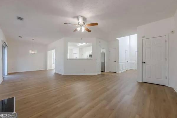 a view of an empty room with wooden floor and a ceiling fan