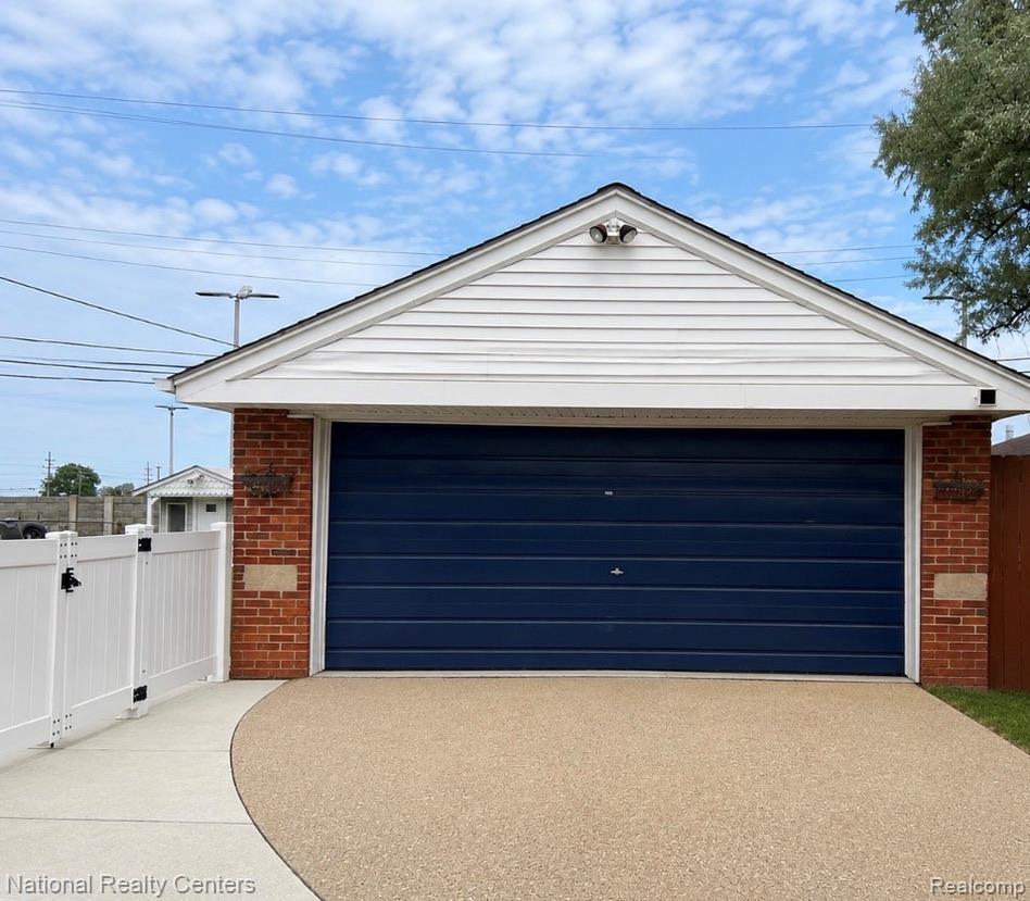 7285 Helen Street Center Line, MI 48015 - Photo 4 of 32 Attached garage with a deep blue sectional door, brick accents, white vinyl siding, and a gabled roofline