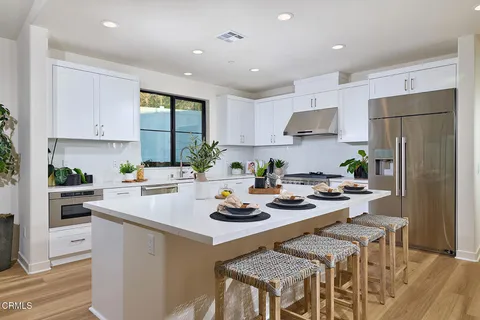 a kitchen with stainless steel appliances granite countertop a stove a refrigerator a sink a stove and white cabinets with wooden floor