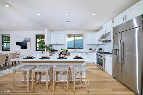 a kitchen with stainless steel appliances kitchen island granite countertop a refrigerator a stove a sink a dining table and chairs