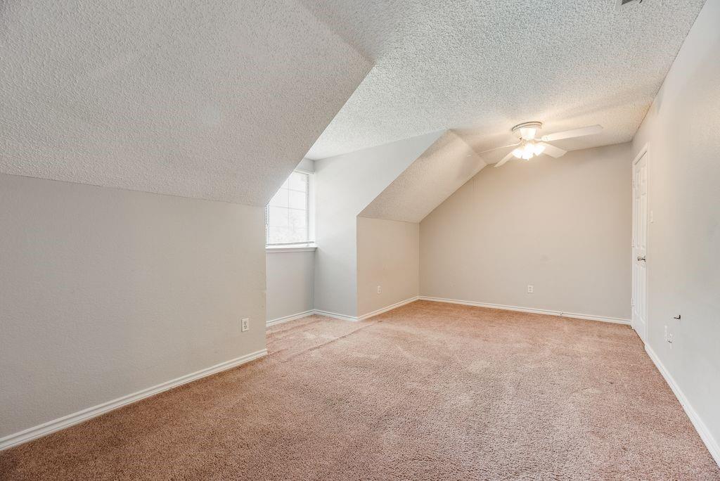 5610 Eagle Rock Road Arlington, TX 76017 - Photo 29 of 33 Spacious room featuring sloped ceilings, a window providing natural light, neutral wall colors, textured carpeting, and a ceiling fan with integrated lighting