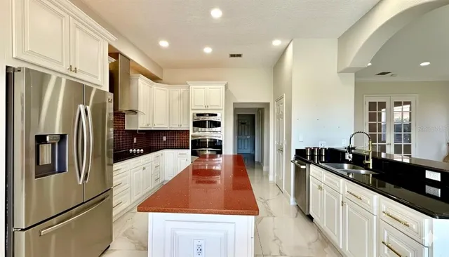 a kitchen with stainless steel appliances granite countertop a refrigerator a sink and white cabinets