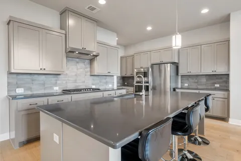 a kitchen with stainless steel appliances granite countertop a refrigerator a stove a sink a dining table and chairs with wooden floor