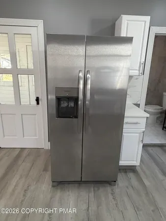 a view of a refrigerator in kitchen and an empty room with wooden floor