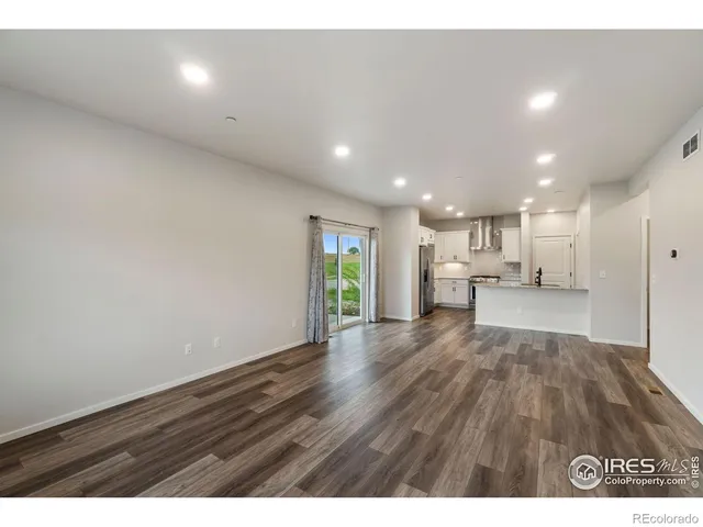 a view of an empty room and kitchen view with wooden floor