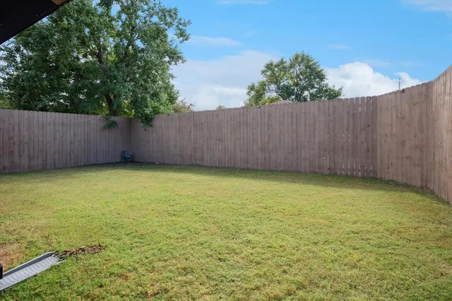a view of a yard with an empty space and wooden fence