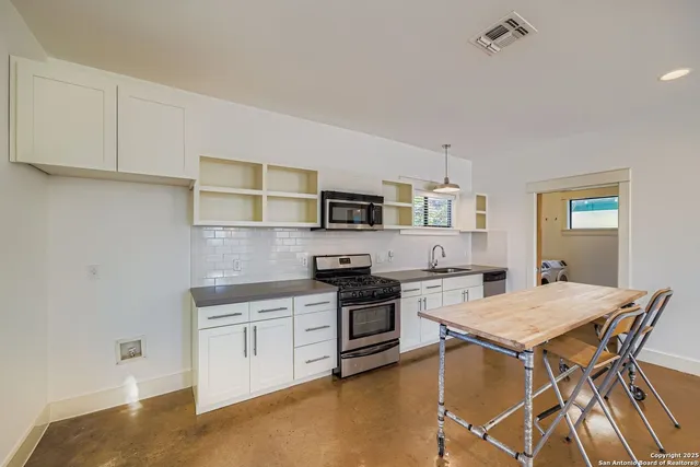 a kitchen with stainless steel appliances granite countertop a stove top oven a sink dishwasher and white cabinets with wooden floor