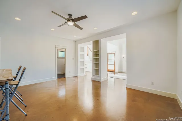 a view of an empty room with wooden floor and a ceiling fan