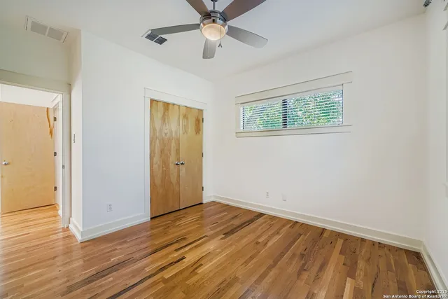 an empty room with wooden floor chandelier fan and windows