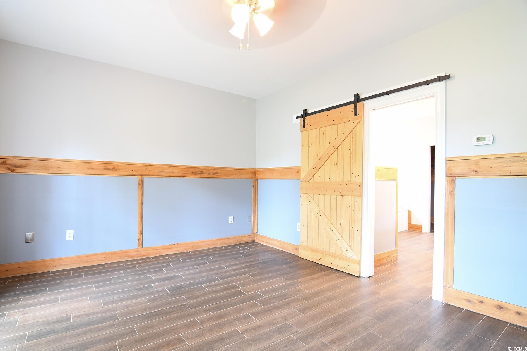 971 Folly Road Myrtle Beach, SC 29588 - Photo 8 of 25 Empty room with a barn door, ceiling fan, baseboards, and wood finished floors
