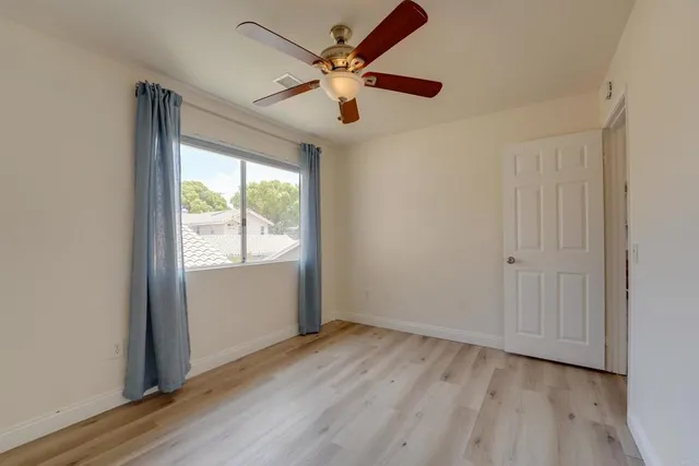 an empty room with wooden floor fan and windows