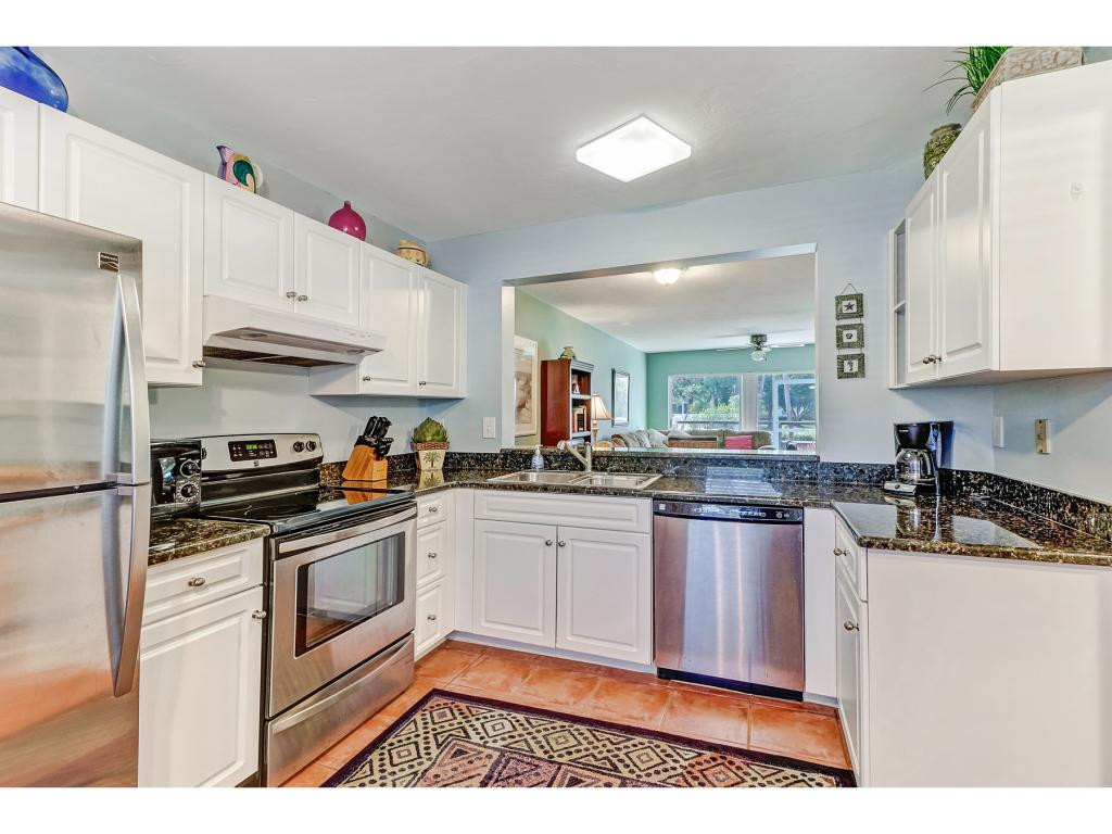 5739 Whitaker Road, Unit 103 Naples, FL 34112 - Photo 9 of 18 a kitchen with granite countertop a sink stainless steel appliances and white cabinets