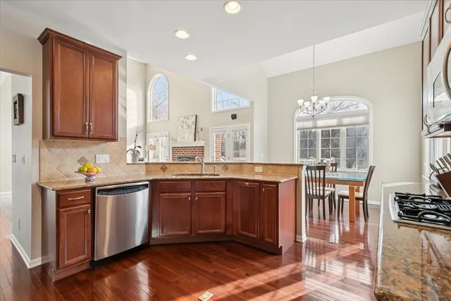 a kitchen with stainless steel appliances granite countertop a stove top oven a sink dishwasher and wooden cabinets with wooden floor